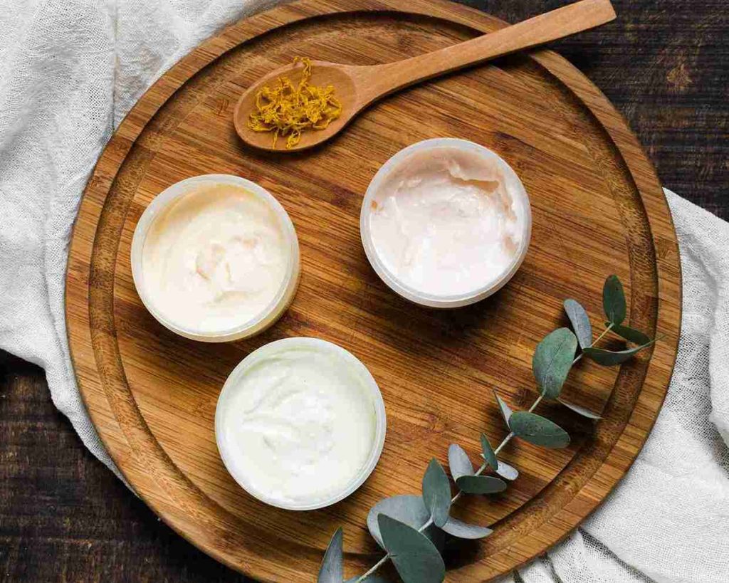 Três potes de creme vegetal e margarina produzidos com óleo de algodão sobre tábua de madeira, enfatizando a textura e aplicação industrial.