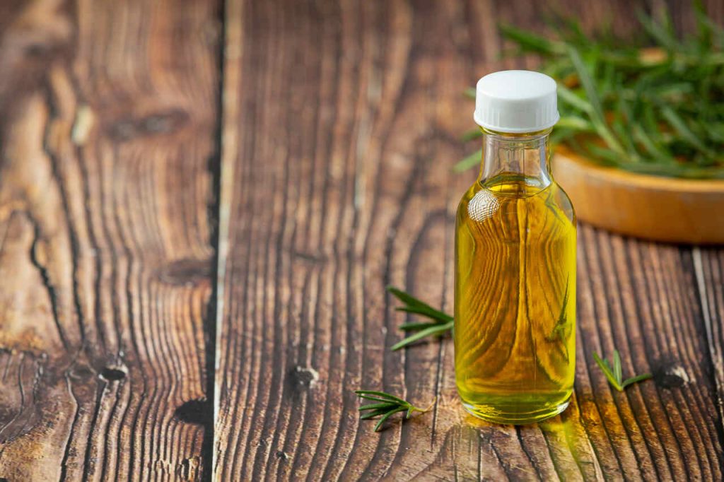 óleo vegetal em garrafa de vidro com ervas aromáticas sobre mesa de madeira rústica