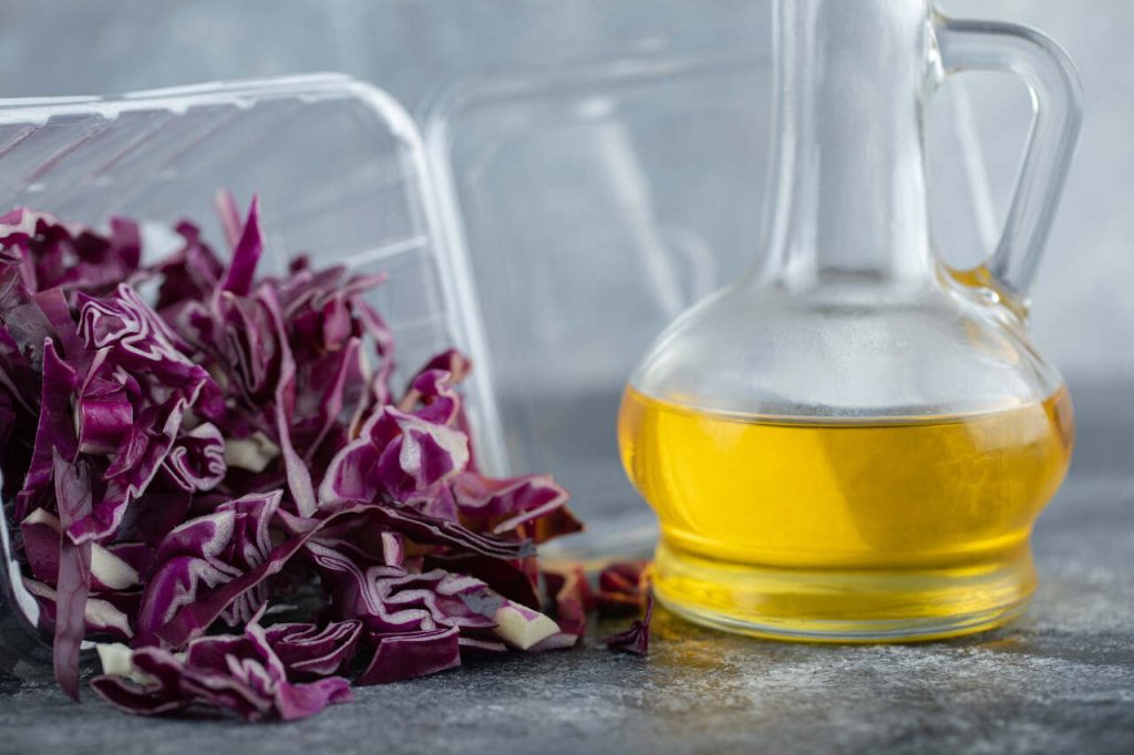 repolho roxo fatiado ao lado de óleo vegetal em recipiente de vidro sobre superfície de cozinha