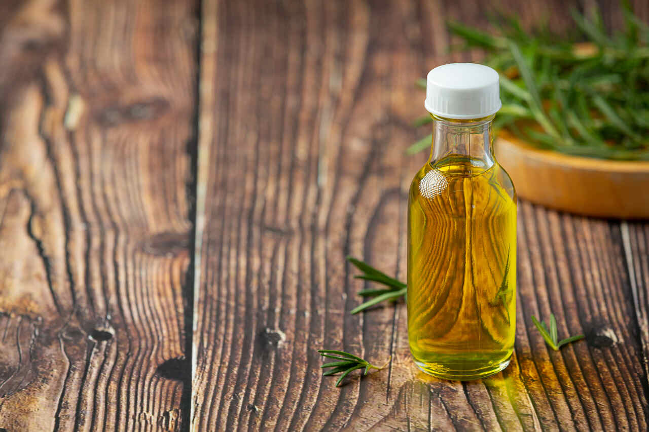 óleo vegetal em garrafa de vidro com ervas aromáticas sobre mesa de madeira rústica
