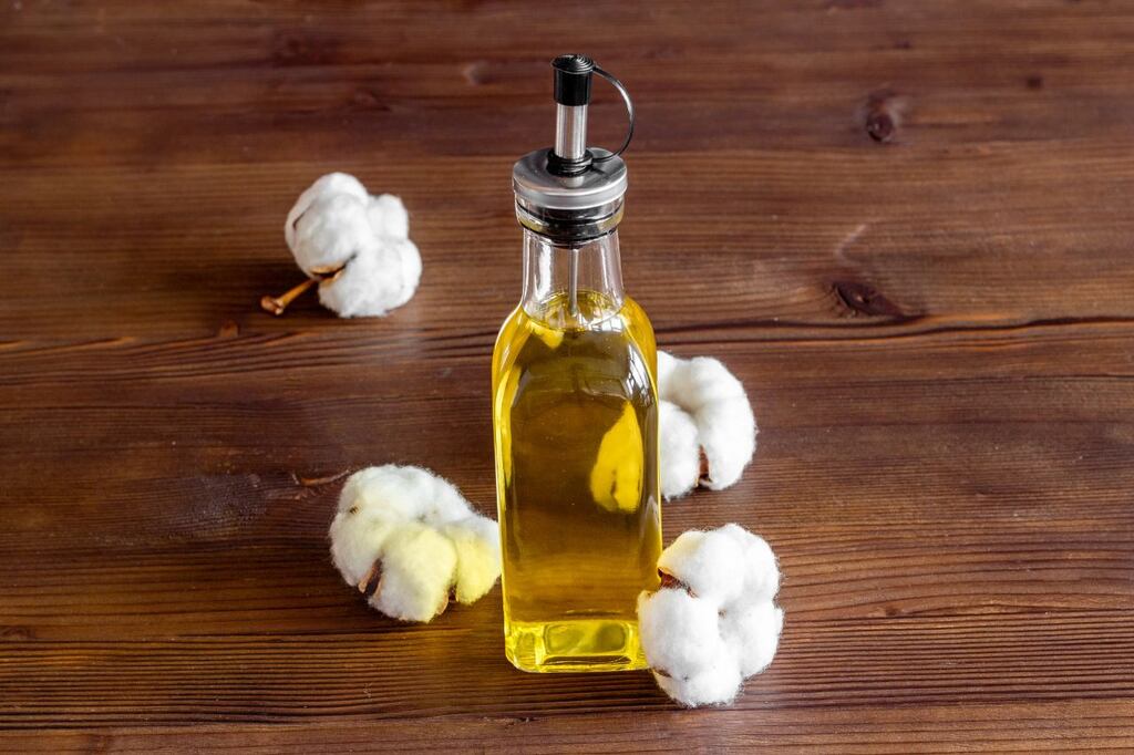 Frasco de óleo de algodão sobre mesa de madeira com algodões ao redor representando armazenamento e durabilidade