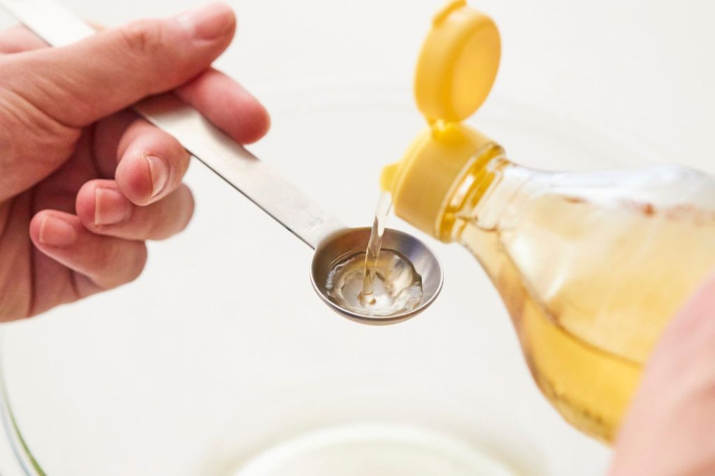 Óleo de algodão sendo despejado em colher medidora durante preparo culinário em cozinha